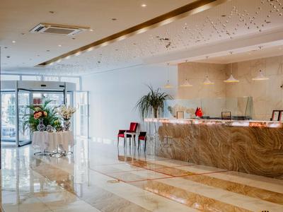 Bright hotel lobby with marble floors, reception desk, plants, and large windows.