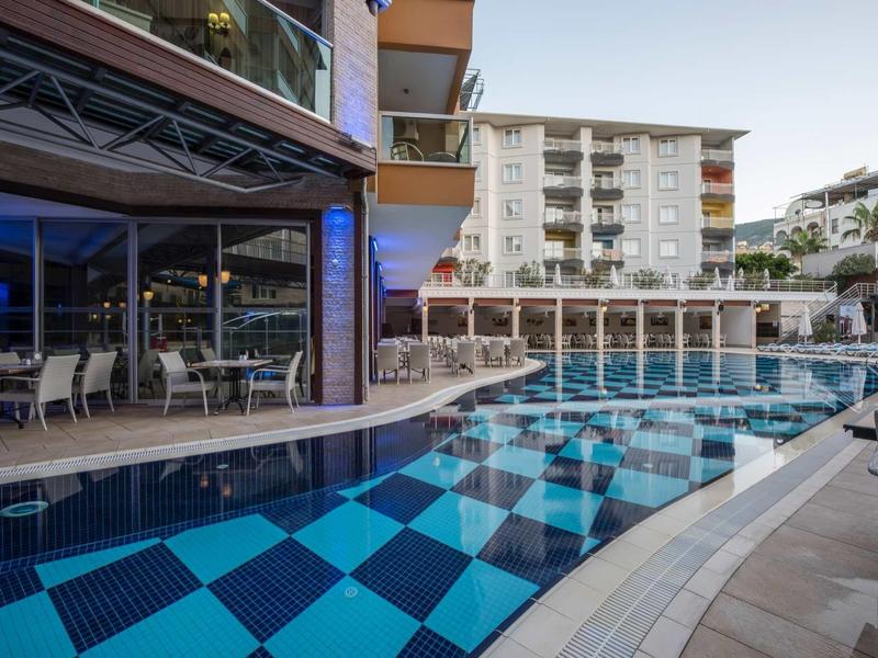 Outdoor pool area with checkered floor, seating, and multi-story hotel in the background.