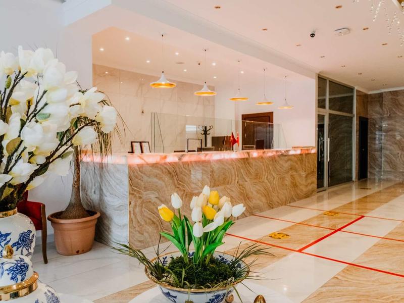 Hotel lobby with marble reception desk, flower pots, and polished floor tiles.