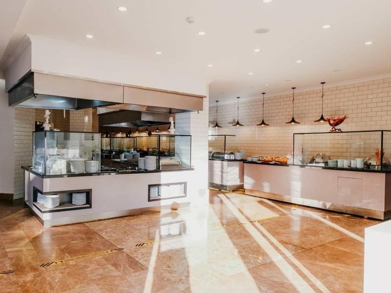 Modern hotel buffet area with glass display counters, warm lighting, and shiny marble flooring.