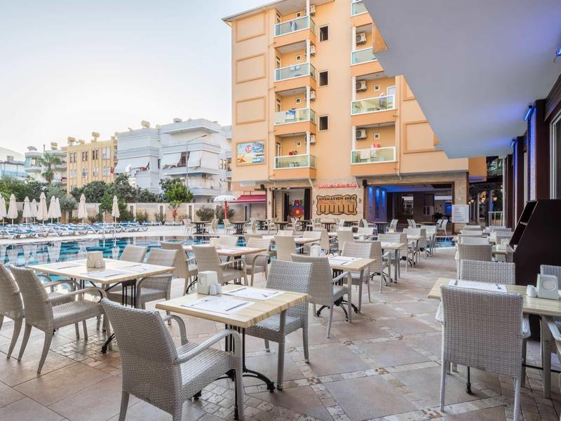 Outdoor dining area with tables and chairs beside a pool in a hotel courtyard at sunset.