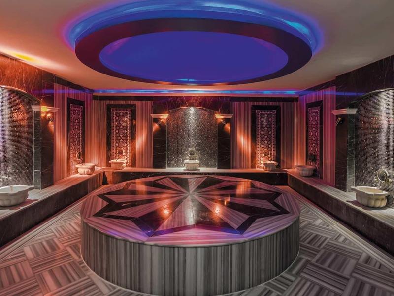 Luxurious spa room with circular central fountain, elegant lighting, and intricate wall designs.