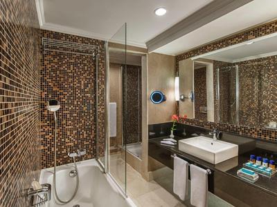 Moderne Badezimmer mit braunen Mosaikfliesen, großer Spiegel, Badewanne und Waschtisch mit weißem Becken.