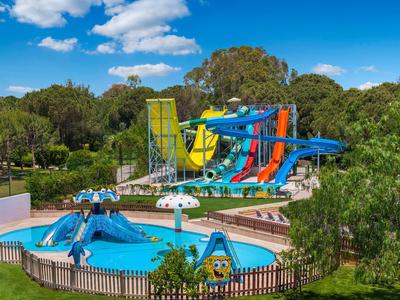 Wasserpark mit bunten Rutschen, Pool und grünem Garten bei blauem Himmel.