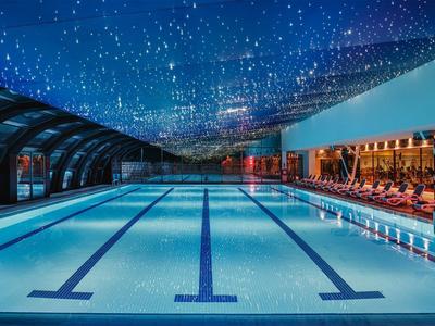 Schwimmbad mit beleuchtetem Sternenhimmel, blauer Wasserfläche und Sitzbereich rechts.