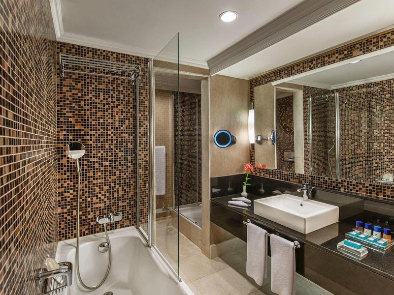 Moderne Badezimmer mit braunen Mosaikfliesen, großer Spiegel, Badewanne und Waschtisch mit weißem Becken.