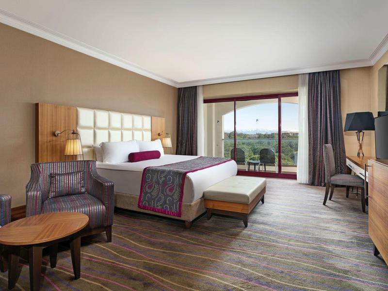 Modernes Hotelzimmer mit großem Bett, Holzmöbeln und Panoramafenster mit Blick ins Grüne.