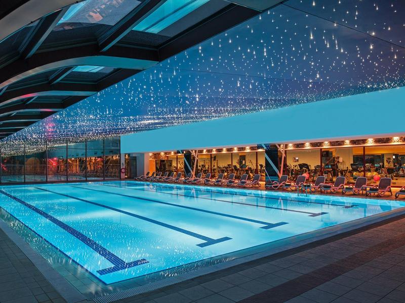 Beleuchtetes Außenbecken mit überdachtem Rand und Sternenhimmel bei Dämmerung.