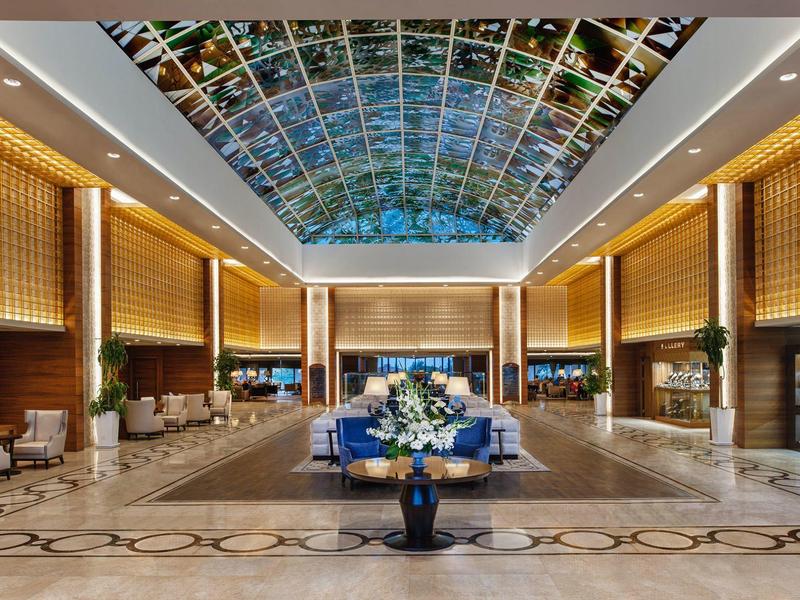 Große Hotellobby mit Marmorfußboden, hohen Decken und buntem Glasdachfenster.