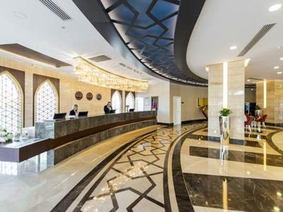 Große Hotellobby mit langem Empfangstresen, glänzendem Marmorfußboden und modernen Deckenelementen.