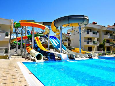 Mehrere bunte Wasserrutschen führen in einen großen blauen Pool vor einem Appartementgebäude.