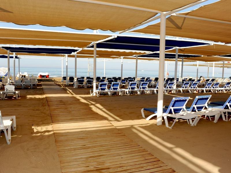 Covered lounge area with blue sunbeds and wooden floor on the beach.