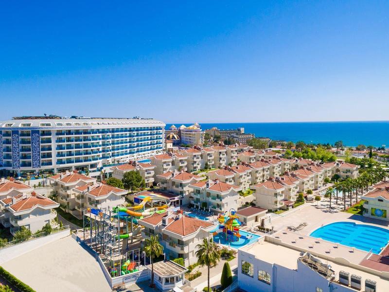 Large resort with pools, water playground, and sea view under clear sky.
