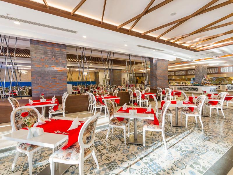 Elegant restaurant with white chairs and red table settings in bright ambiance.