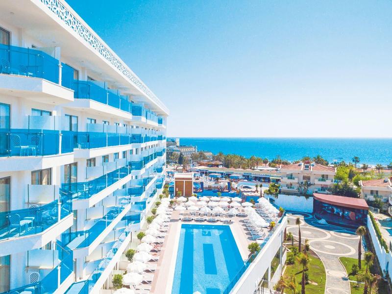 Modern hotel complex with outdoor pool and sea view under clear blue sky.