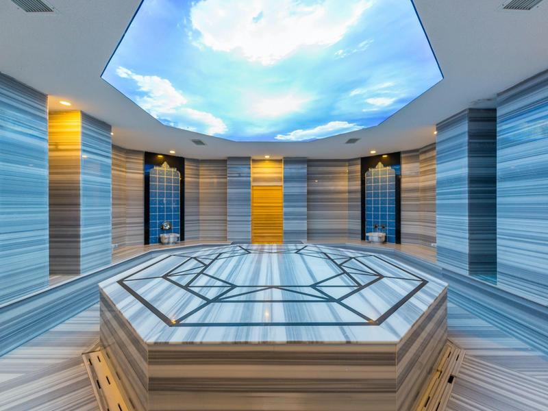 Modern spa room with marble bathtub and illuminated sky ceiling.