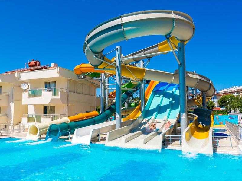Water slide complex next to a pool in front of hotel buildings on a sunny day.