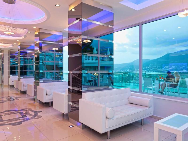 Moderní hotelový salonek s bílými pohovkami a velkými okny s výhledem na hory.
