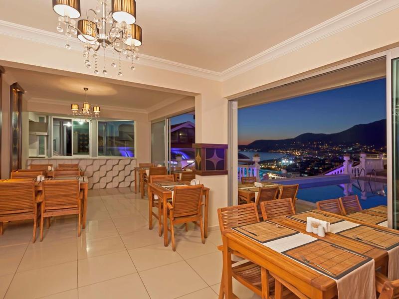 Příjemná restaurace s dřevěnými stoly a výhledem na noční město a bazén.