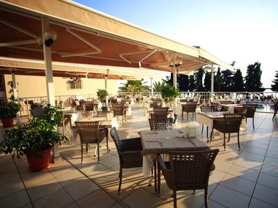 Een zonnig buitenterras met veel tafels en stoelen bij een hotel.