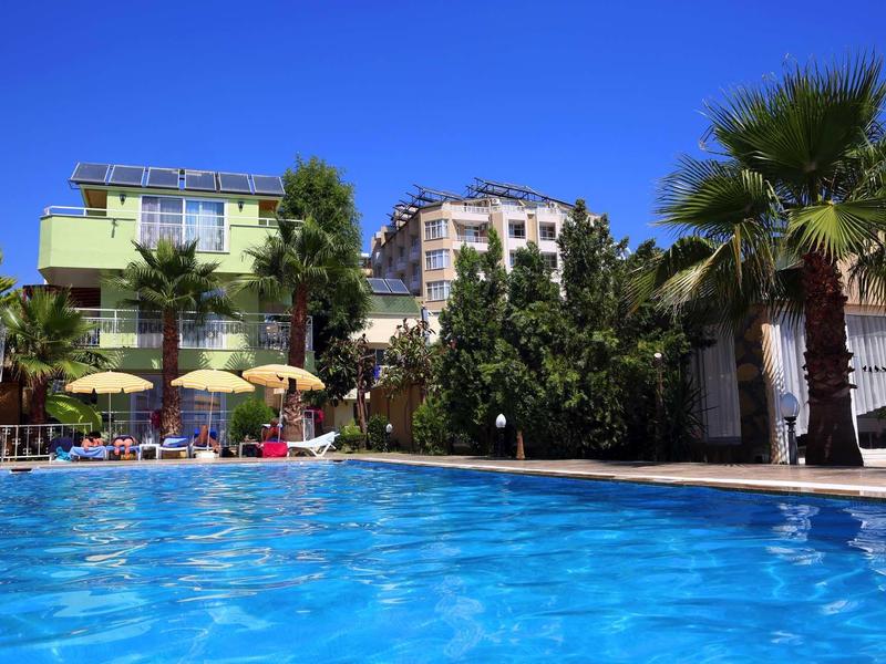 Lichtgroen hotel met blauw zwembad en palmbomen onder een heldere blauwe lucht