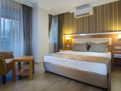 Chambre d'hôtel moderne avec grand lit, fauteuil, table et fenêtre avec rideaux.