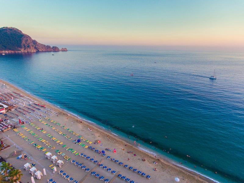 Vue sur une large plage de sable avec des parasols colorés et une mer bleue calme