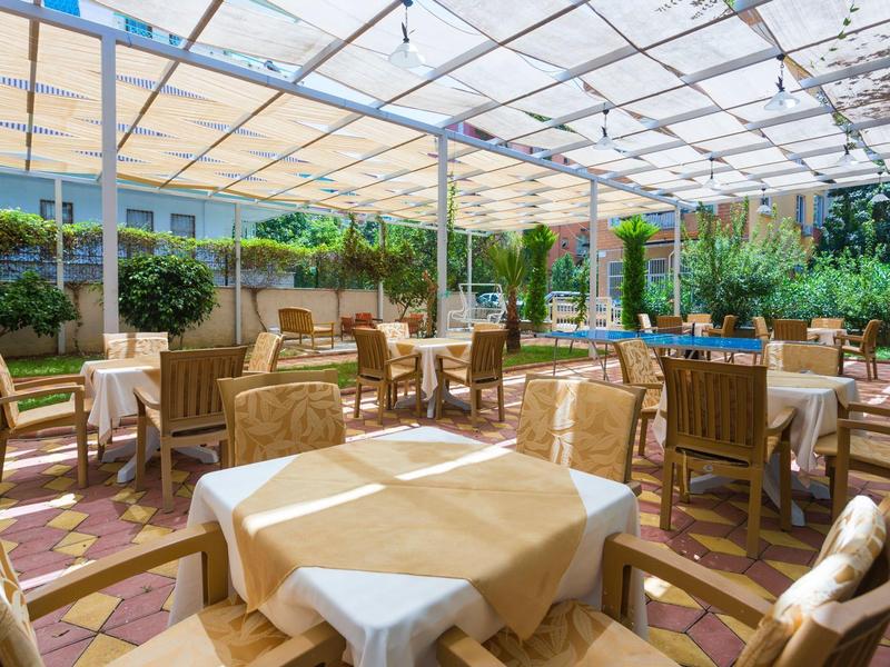 Salon terrasse couverte avec tables et chaises dans un jardin d'hôtel.