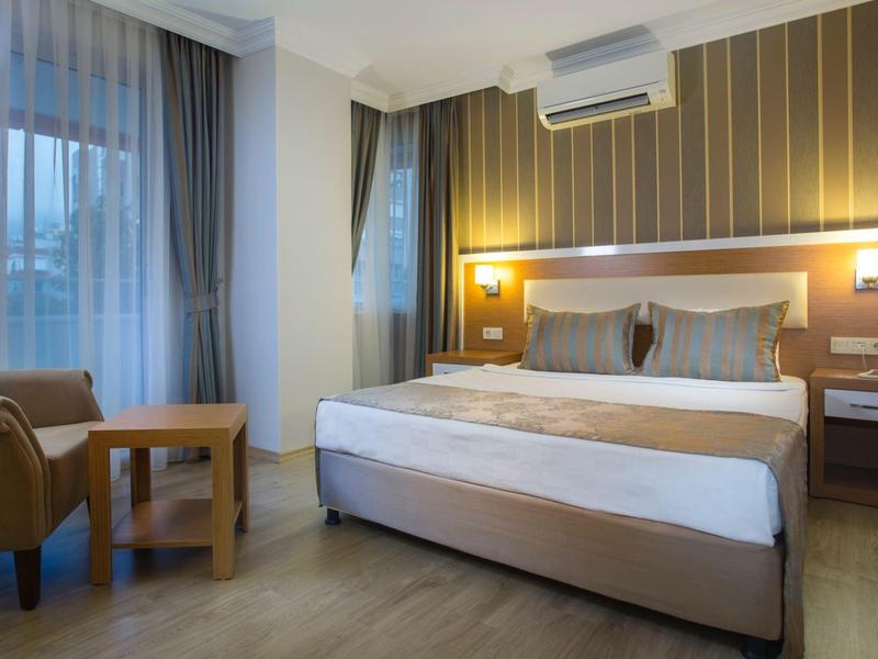 Chambre d'hôtel moderne avec lit double, fauteuil, tables de chevet et grande fenêtre avec rideaux.