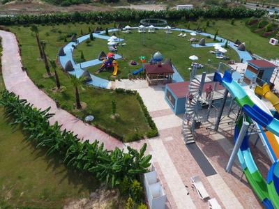 Großer, runder Wasserpark mit bunten Rutschen, grünen Liegewiesen und umliegenden Wegen und Pflanzen.