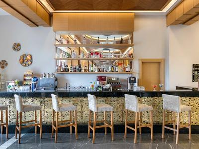 Moderne Bar mit sechs Holzstühlen und beleuchtetem Tresen, Bücherregal und Kunst an weißen Wänden.