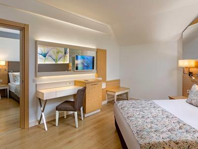 Modern eingerichtetes Schlafzimmer mit Doppelbett, Fernseher, Schreibtisch und Holzboden.