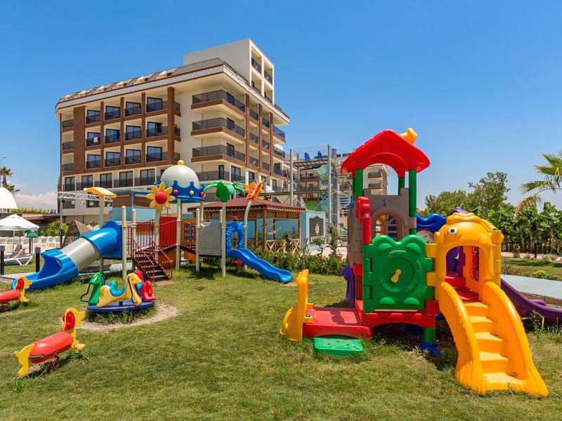 Colorful children's playground with slides and climbing frames in front of a modern hotel under clear sky.