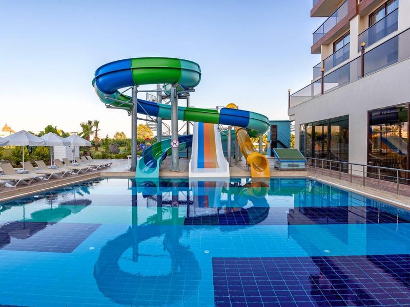 Colorful water slides next to a hotel pool under a clear sky.