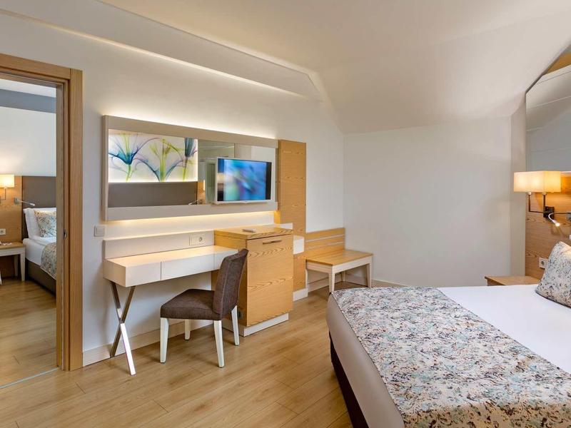 Bright hotel room with double bed, desk, chair, and large mirror.