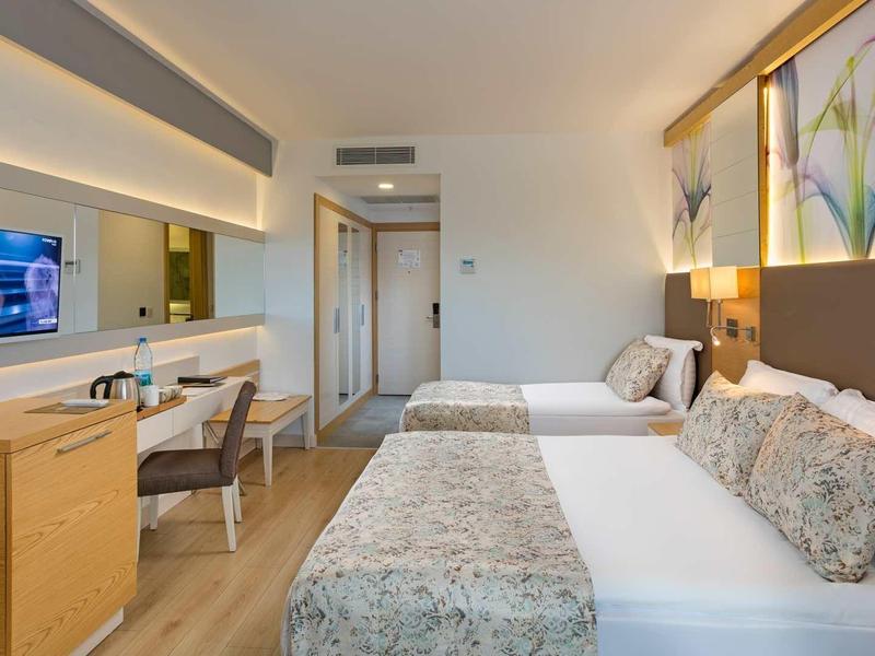 Modern hotel room with two beds, desk, and large mirror.