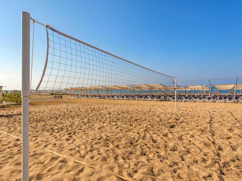Empty volleyball net on sandy beach with sun loungers and clear blue sky