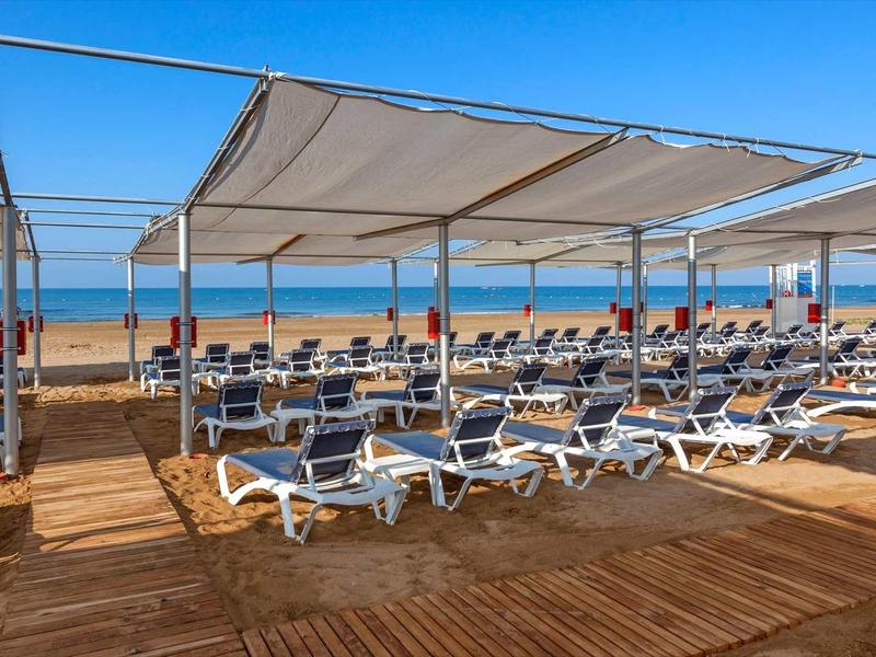 Beach with sun loungers and umbrellas under a white canopy by the sea.