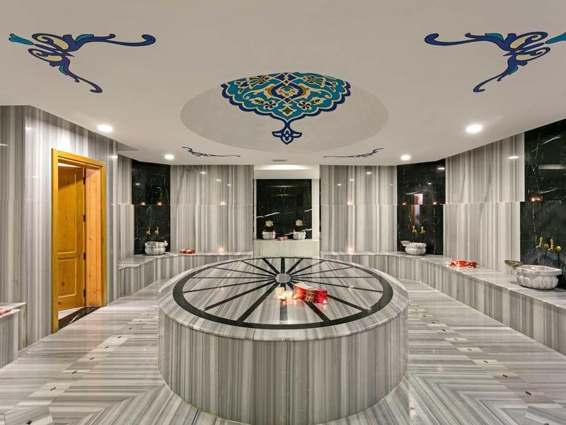 Modern hammam with gray marble, central round stone, and wall art on the ceiling.