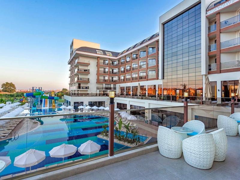 Modern hotel pool with white umbrellas and seating at sunset.