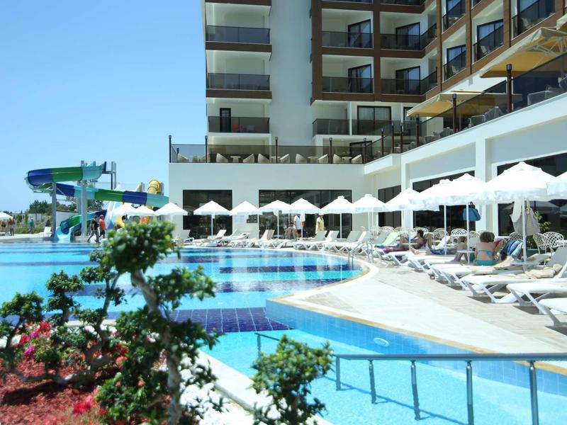 Hotel pool with water slides, sun loungers, and umbrellas under clear sky
