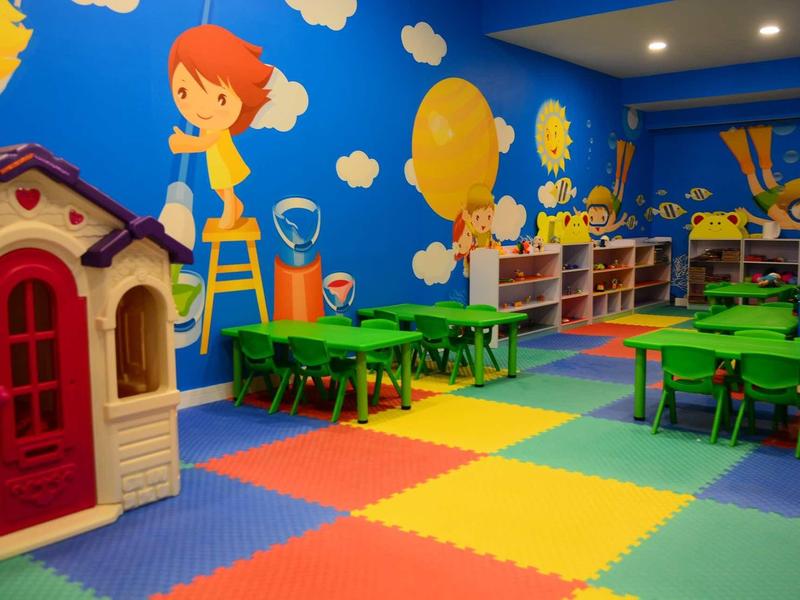 Colorful kids' playroom with playhouse, green tables, chairs, and wall paintings.