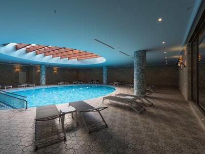 Moderner Innenpool mit großen Fenstern, Liegestühlen und einem ockerfarbenen Deckenfenster.