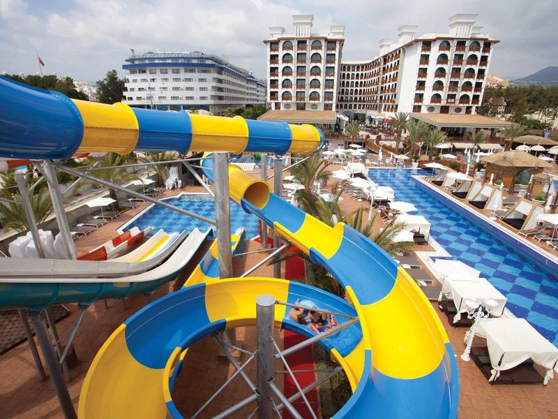 Wasserpark mit bunten Wasserrutschen und Liegestühlen neben einem großen Hotelkomplex.