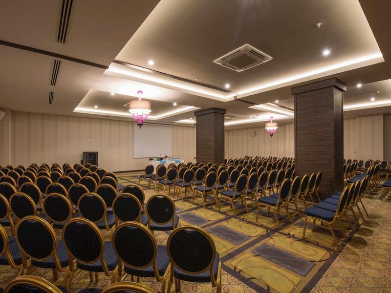 Großer Konferenzraum mit vielen blauen Stühlen, Teppichboden und indirekter Deckenbeleuchtung.