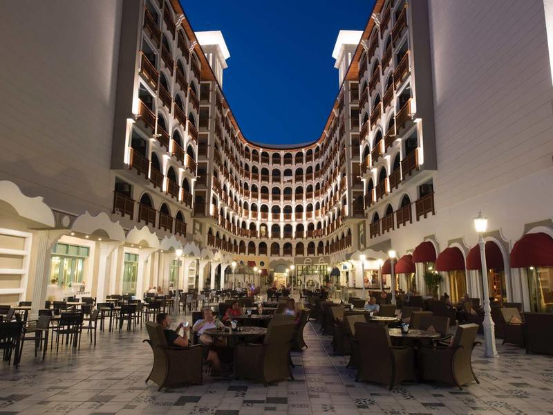 Großer Innenhof eines Hotels mit Stühlen, Tischen, Arkaden und dunklem Nachthimmel.