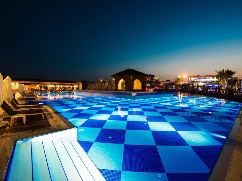 Beleuchteter Schwimmbad mit blau-weißem Schachbrettmuster und Liegestühlen bei Nacht.