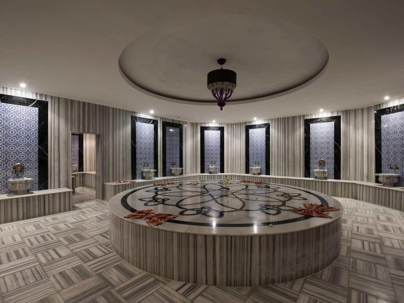 Großer runder Raum mit Marmorbecken, verzierten Kacheln und elegantem Kronleuchter an der Decke.