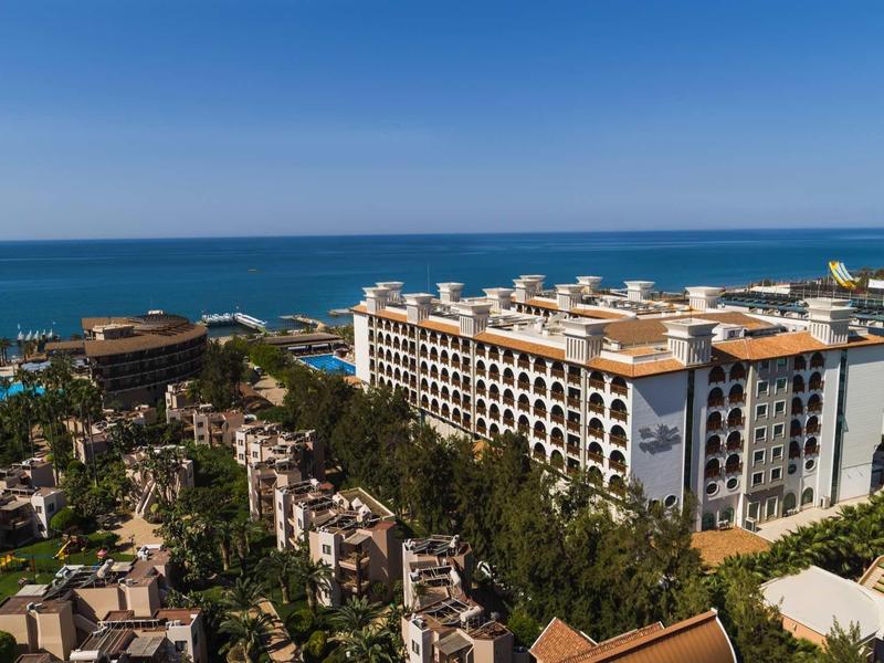 Großes Hotel an der Küste mit vielen Bäumen und blauem Himmel über dem Meer.