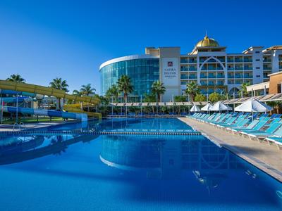 Moderní hotelový bazén s lehátky a palmami pod jasnou oblohou.